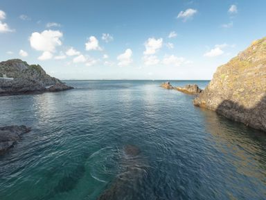 A coastal scene with clear water between rocky cliffs under a partly cloudy sky at Nectan in Mevagissey