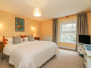 A bedroom with a large bed two bedside tables a window with curtains and a television on a white dresser at The Well House Apartment in Watchet