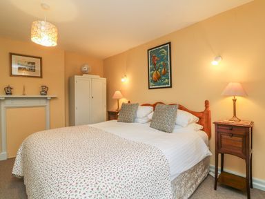A bedroom with a double bed bedside tables lamps a wardrobe and framed pictures at The Well House Apartment in Watchet