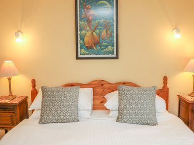 A bedroom with a wooden bed and patterned pillows a framed painting and two bedside tables with lamps at The Well House Apartment in Watchet