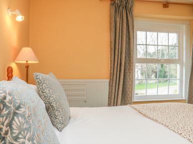 A bedroom with a bed and two decorative pillows near a window with curtains at The Well House Apartment in Watchet