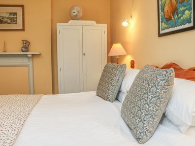 A bedroom with a bed with patterned pillows a white wardrobe a lamp and framed pictures at The Well House Apartment in Watchet