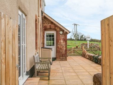 An outdoor patio area with a wooden bench stone walls and a gate leading to a grassy field at The Well House Apartment in Watchet
