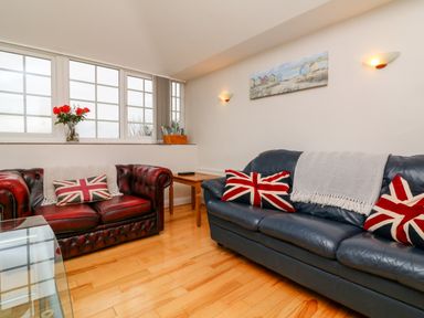 A living room with two leather sofas with union jack pillows and a wooden floor at The Well House Apartment in Watchet
