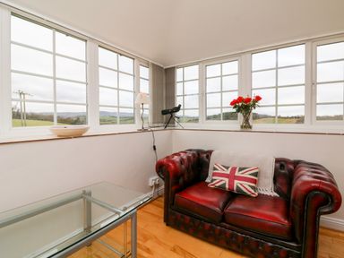 A sitting area with a red leather sofa a pillow with a union jack a glass table and large windows at The Well House Apartment in Watchet