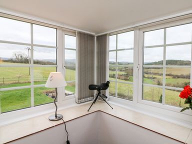 A corner window with a lamp, binoculars on a tripod, and a vase with red flowers at The Well House Apartment in Watchet
