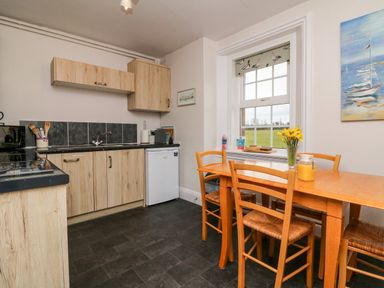 A kitchen with wooden cabinets a dining table with chairs and a vase of yellow flowers by a window at The Well House Apartment in Watchet