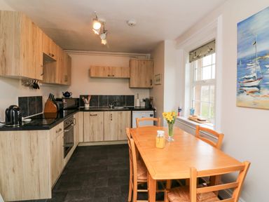A kitchen with wooden cabinets a black countertop and a wooden dining table with chairs and flowers at The Well House Apartment in Watchet