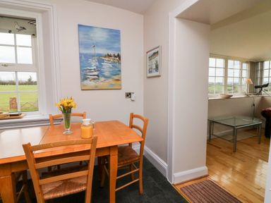 A dining area with a wooden table and chairs near a window with a vase of flowers and a jug at The Well House Apartment in Watchet