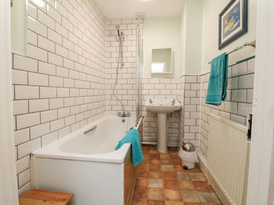 A bathroom with a bathtub shower combination a pedestal sink towel rail with a towel and a framed picture above the radiator at The Well House Apartment in Watchet