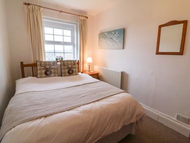 A bedroom with a double bed two deer design pillows lamp on a bedside table and a window with curtains at The Well House Apartment in Watchet