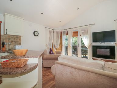 A living room with sofas a wall-mounted television and a kitchen counter at Bramley Lodge in Hewish near Weston-super-Mare