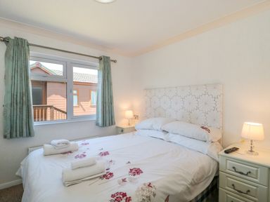 A bedroom with a double bed two bedside tables with lamps and a window with curtains at Bramley Lodge in Hewish near Weston-super-Mare