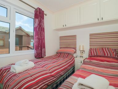 A bedroom with two single beds with striped bedding a window with curtains and overhead cabinets at Bramley Lodge in Hewish near Weston-super-Mare
