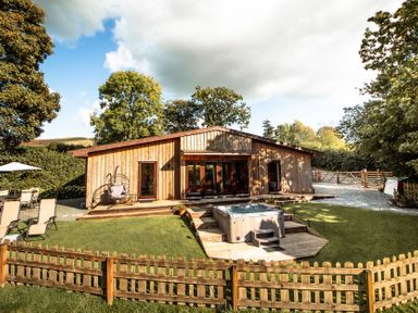 A wooden lodge with a hot tub and garden chairs at Sycamore Lodge Nantmel near Rhayader