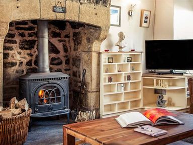 A room with a wood burning stove in a stone fireplace wooden coffee table with an open book shelving unit and a television at Bastle House in Haltwhistle near Hadrians Wall