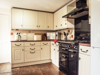 A kitchen with cream cabinets a black stove and oven a microwave and countertop appliances at Bastle House in Haltwhistle near Hadrians Wall