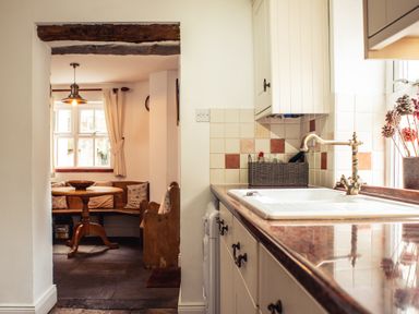 A kitchen sink and counter next to a small dining nook with a round table and bench seating at Bastle House in Haltwhistle near Hadrians Wall
