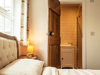 A bedroom with a bedside table lamp curtain and an open door showing a bathroom sink at Bastle House Haltwhistle near Hadrians Wall