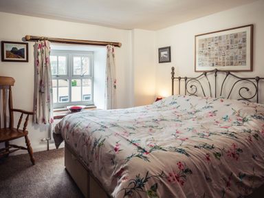 A bedroom with a double bed covered with floral bedding and a wooden chair next to a window at Bastle House in Haltwhistle near Hadrians Wall