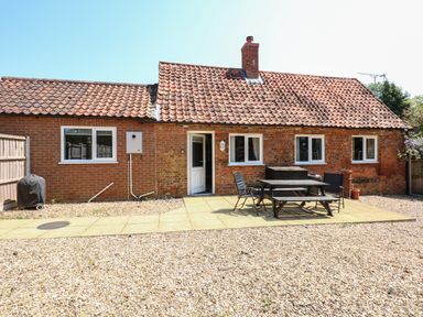A brick house with a tiled roof and a patio area with a table and chairs at Hadleigh Farm Cottage in Gayton
