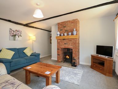 A living room with a wooden coffee table a blue sofa a brick fireplace with a wood stove and a TV on a wooden stand at Hadleigh Farm Cottage in Gayton