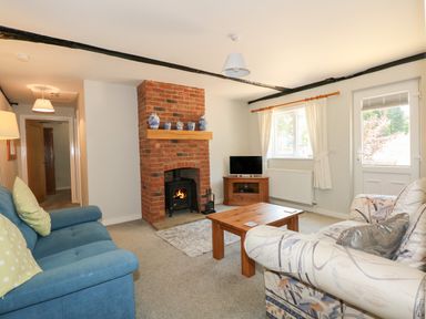 A living room with a brick fireplace two sofas a wooden coffee table and a TV at Hadleigh Farm Cottage in Gayton