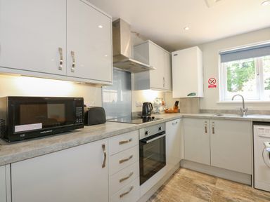 A kitchen with white cabinets a microwave toaster kettle oven and a window at Hadleigh Farm Cottage in Gayton