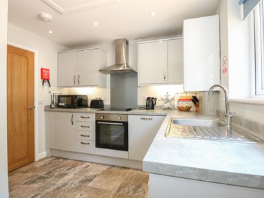 A kitchen with a wooden door gray cabinets an oven microwave toaster kettle sink and countertop at Hadleigh Farm Cottage in Gayton
