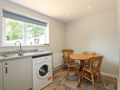 A kitchen area with a washing machine under a countertop and a wooden dining table with four chairs at Hadleigh Farm Cottage in Gayton