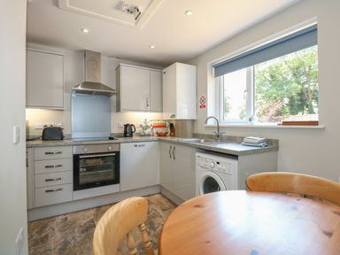 A kitchen with white cabinets a stainless steel oven a washing machine and a wooden dining table at Hadleigh Farm Cottage in Gayton