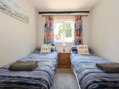A bedroom with two single beds and a window with patterned curtains at Hadleigh Farm Cottage in Gayton