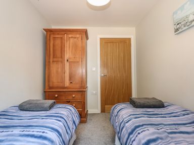 A bedroom with two single beds covered with striped blankets and gray towels a wooden wardrobe and a wooden door at Hadleigh Farm Cottage in Gayton