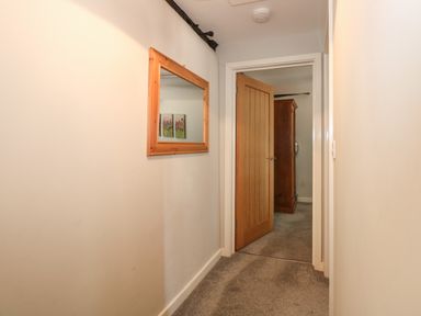 A narrow hallway with a wooden framed mirror on the wall and an open wooden door showing a wardrobe inside a room at Hadleigh Farm Cottage in Gayton