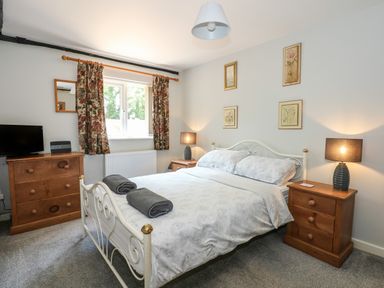 A bedroom with a double bed two bedside tables with lamps a chest of drawers and a window with floral curtains at Hadleigh Farm Cottage in Gayton