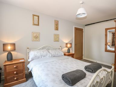 A bedroom with a double bed, bedside tables with lamps, a wooden door and framed pictures at Hadleigh Farm Cottage in Gayton