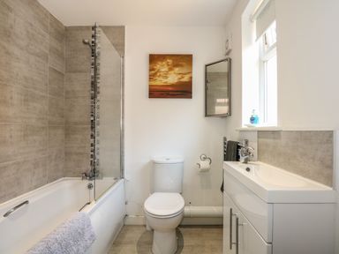 A bathroom with a bathtub shower combination a toilet a sink and a mirror at Hadleigh Farm Cottage in Gayton