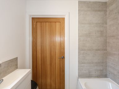 A bathroom with a wooden door a white sink with a gray backsplash and a bathtub with tiled walls at Hadleigh Farm Cottage in Gayton