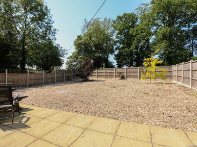 A backyard with gravel ground, a few small trees, wooden fencing and outdoor chairs at Hadleigh Farm Cottage in Gayton