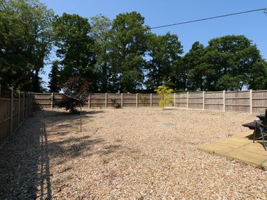 A fenced backyard garden with gravel ground and a few small trees and a rotary clothesline at Hadleigh Farm Cottage in Gayton