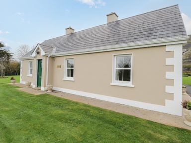 A beige house with a green door and white-framed windows on a grassy lawn at Tieve Baun in Ballintrillick near Kinlough County Sligo