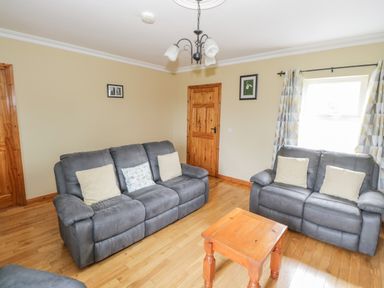 A living room with two gray sofas, a wooden coffee table, window with patterned curtains and framed pictures on walls at Tieve Baun Ballintrillick near Kinlough County Sligo
