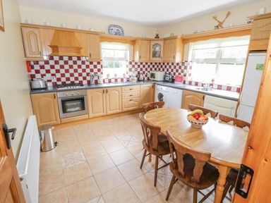 A kitchen with wooden cabinets a dining table with chairs and appliances at Tieve Baun in Ballintrillick near Kinlough County Sligo