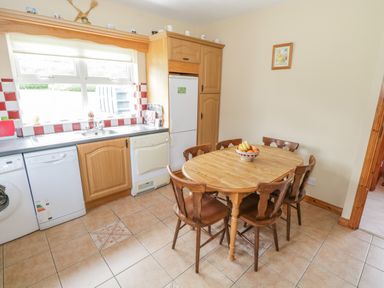 A kitchen with wooden cabinets a round wooden table with six chairs and a bowl of fruit at Tieve Baun Ballintrillick near Kinlough County Sligo