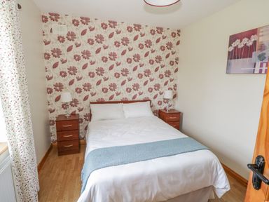 A bedroom with a double bed between two wooden nightstands with lamps and floral wallpaper at Tieve Baun in Ballintrillick near Kinlough County Sligo