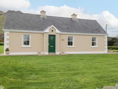 A beige house with a green door and four white windows on a grassy lawn at Tieve Baun in Ballintrillick near Kinlough County Sligo