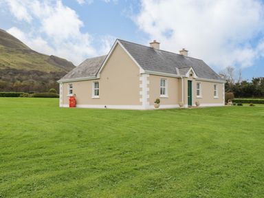 A single story beige house with a gray roof and green door on a grassy lawn at Tieve Baun Ballintrillick near Kinlough County Sligo