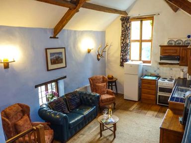 A living area with leather and upholstered chairs a small round table with wine glasses a kitchen with white refrigerator stove and wooden cabinets at The Mill in Bicknoller