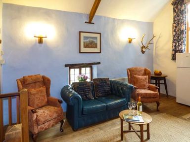A living room with two armchairs a blue sofa a small round table with wine glasses and a bottle and a refrigerator at The Mill in Bicknoller
