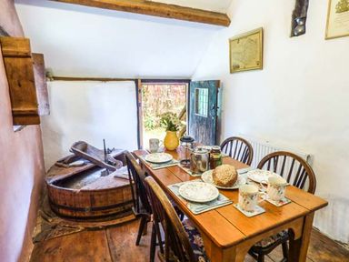 A wooden dining table set with plates cups and a loaf of bread in a room with wooden beams and an open door at The Mill in Bicknoller